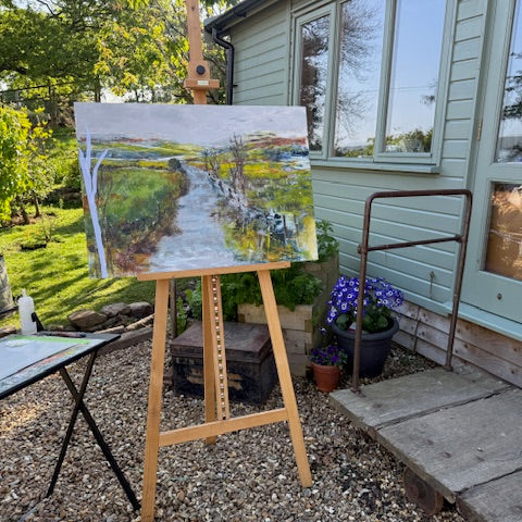 Painting of a landscape on an easel outdoors with a house and garden in the background
